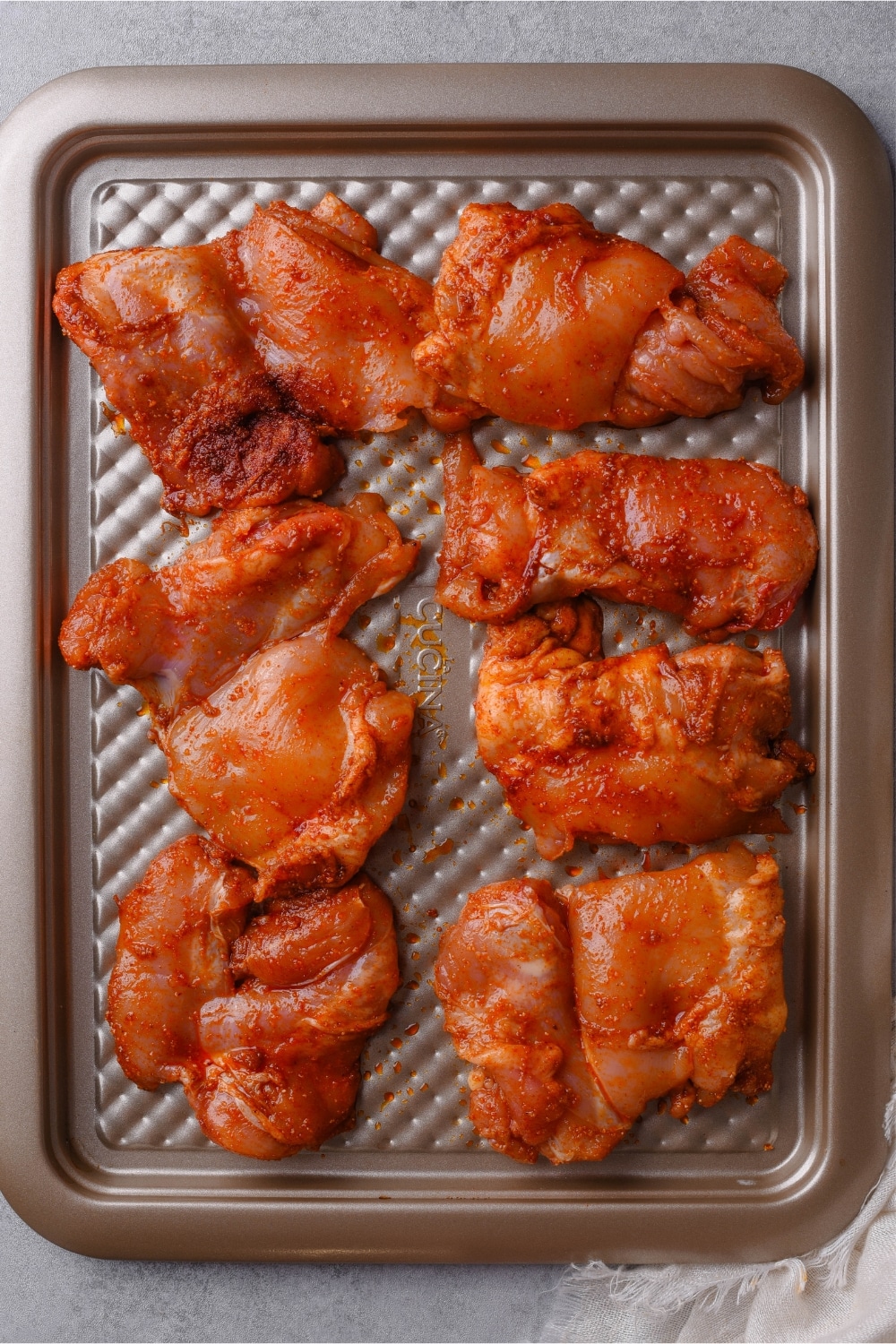 Seasoned raw boneless skinless chicken thighs on a baking sheet.
