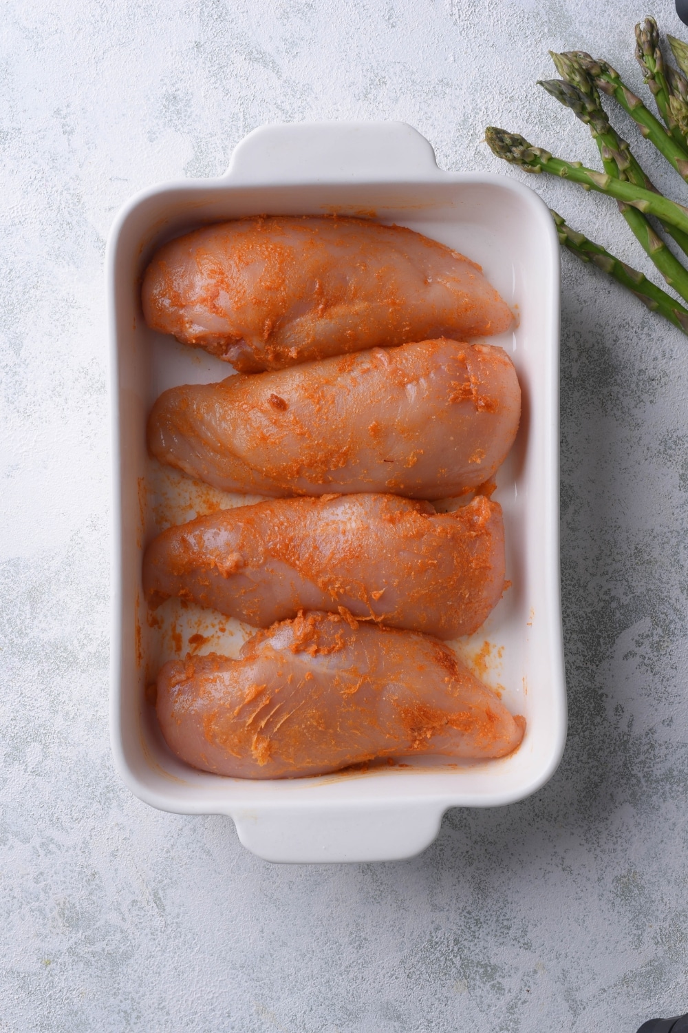 Four raw seasoned chicken breasts in a baking tray.