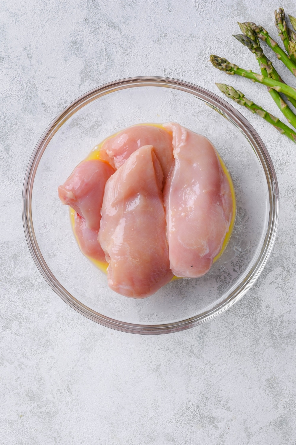Raw chicken breasts and melted butter in a glass bowl.