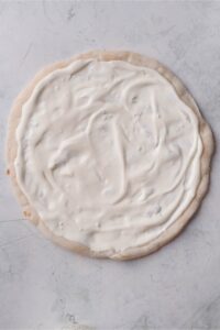 Pizza dough covered in the creamy dill pickle pizza base.
