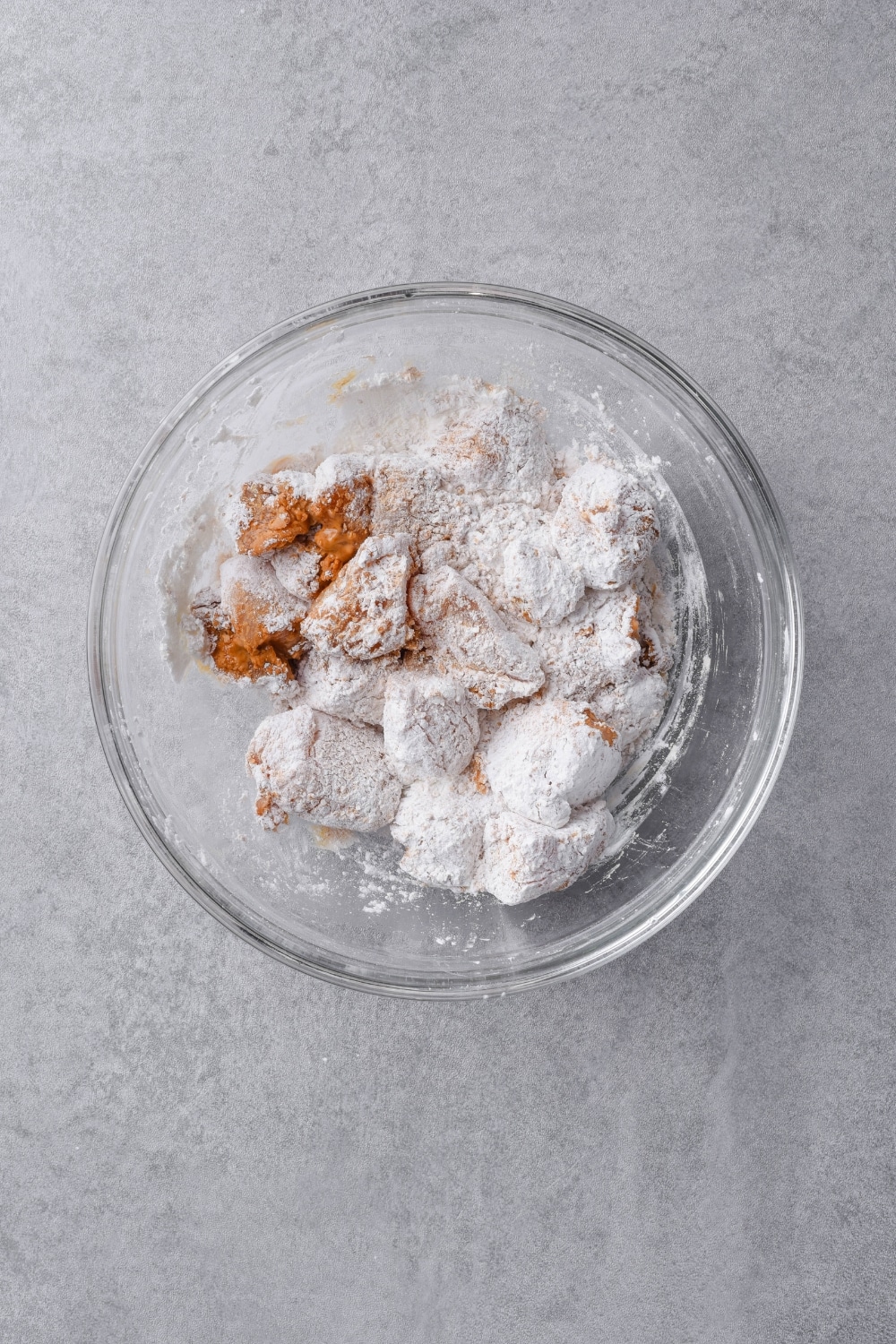 Chicken breast pieces coated in cornstarch in a glass bowl.