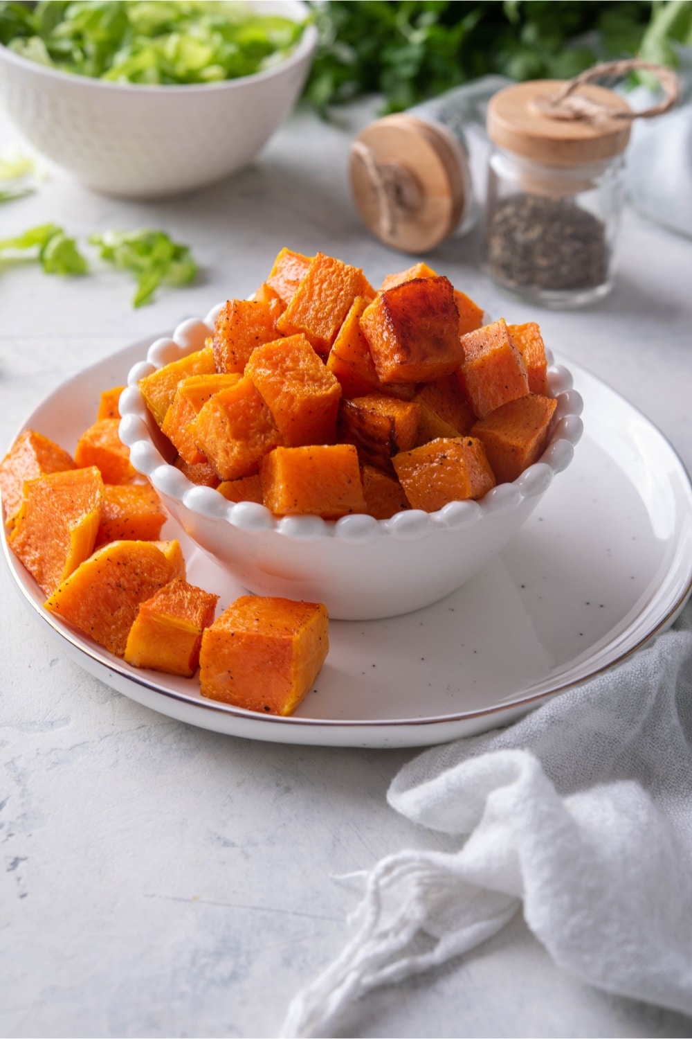 Roasted butternut squash in a white bowl next to a bowl of salad greens.