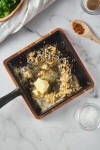 Butter being melted on a square cast iron pan with minced garlic.