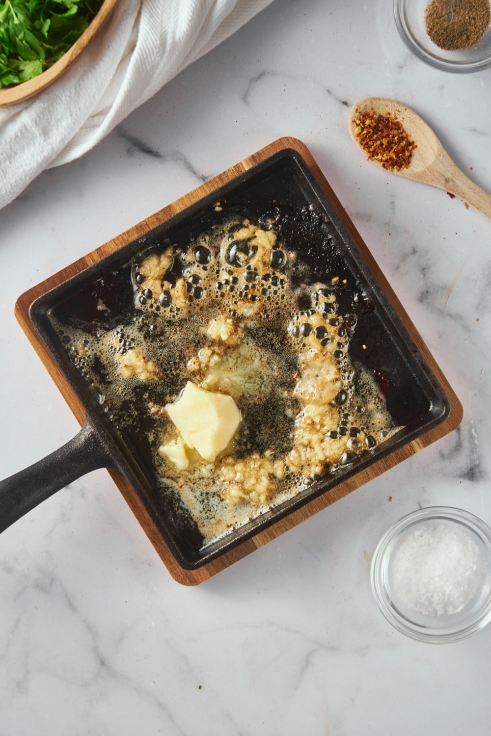 Butter being melted on a square cast iron pan with minced garlic.