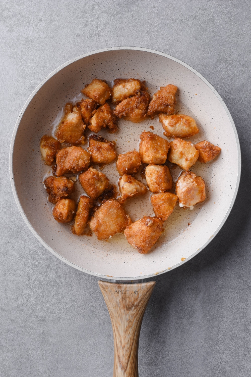 Fried chicken breast pieces in oil in a white skillet with a wooden handle.