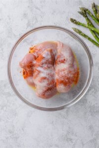 Raw chicken breasts coated in seasonings and melted butter in a glass bowl.