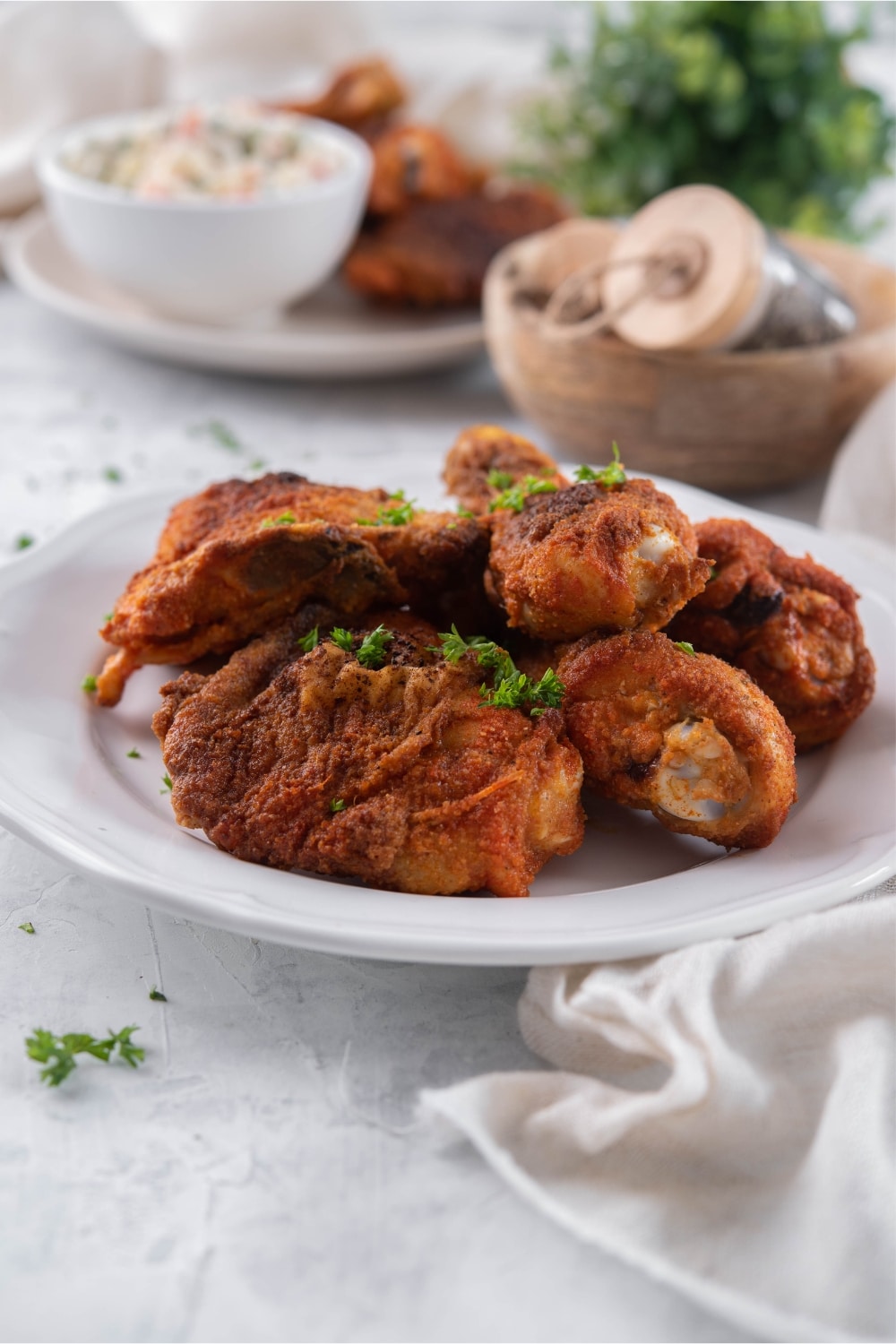 A plate of baked chicken legs and thighs. In the back is another plate of chicken legs and thighs served with a creamy salad.
