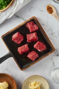 Raw steak bites on a square cast iron pan.