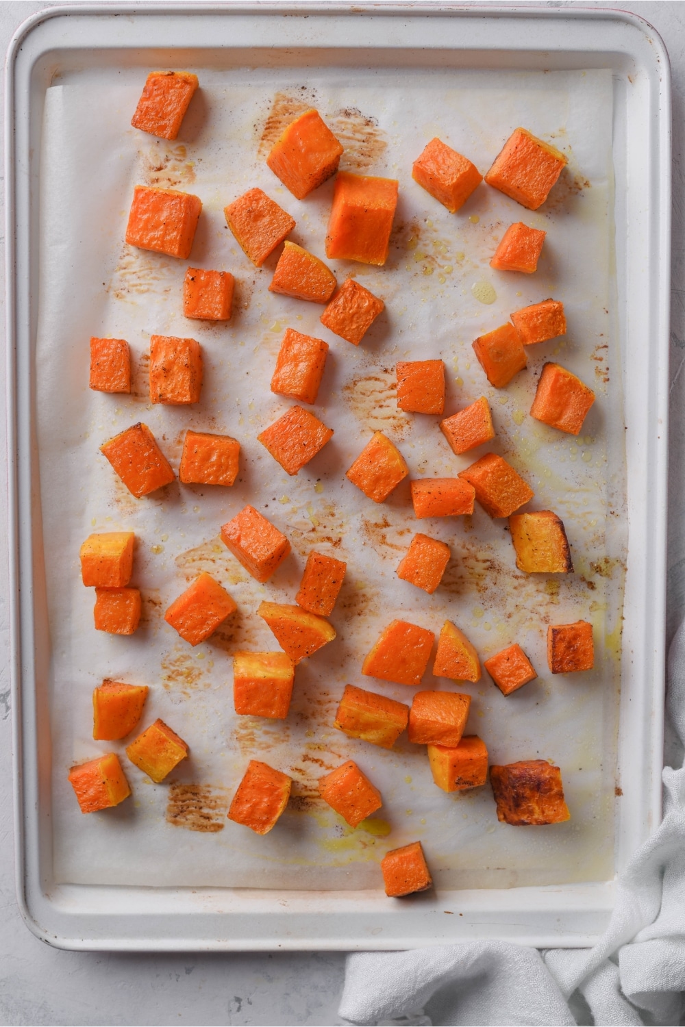 Roasted butternut squash cubes spread out on a parchment paper-lined baking sheet.