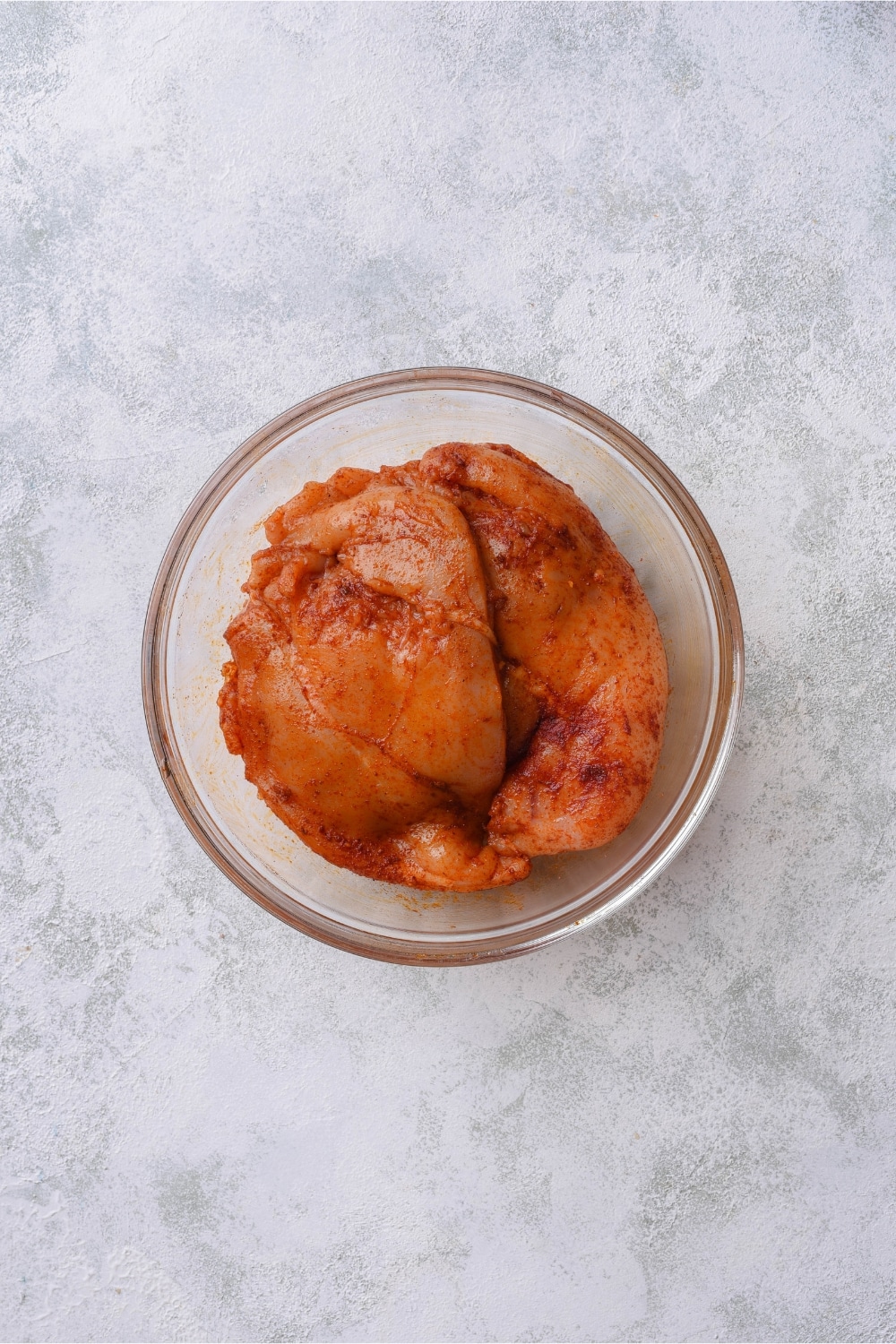 Thin chicken breasts covered with seasoning in a glass bowl.