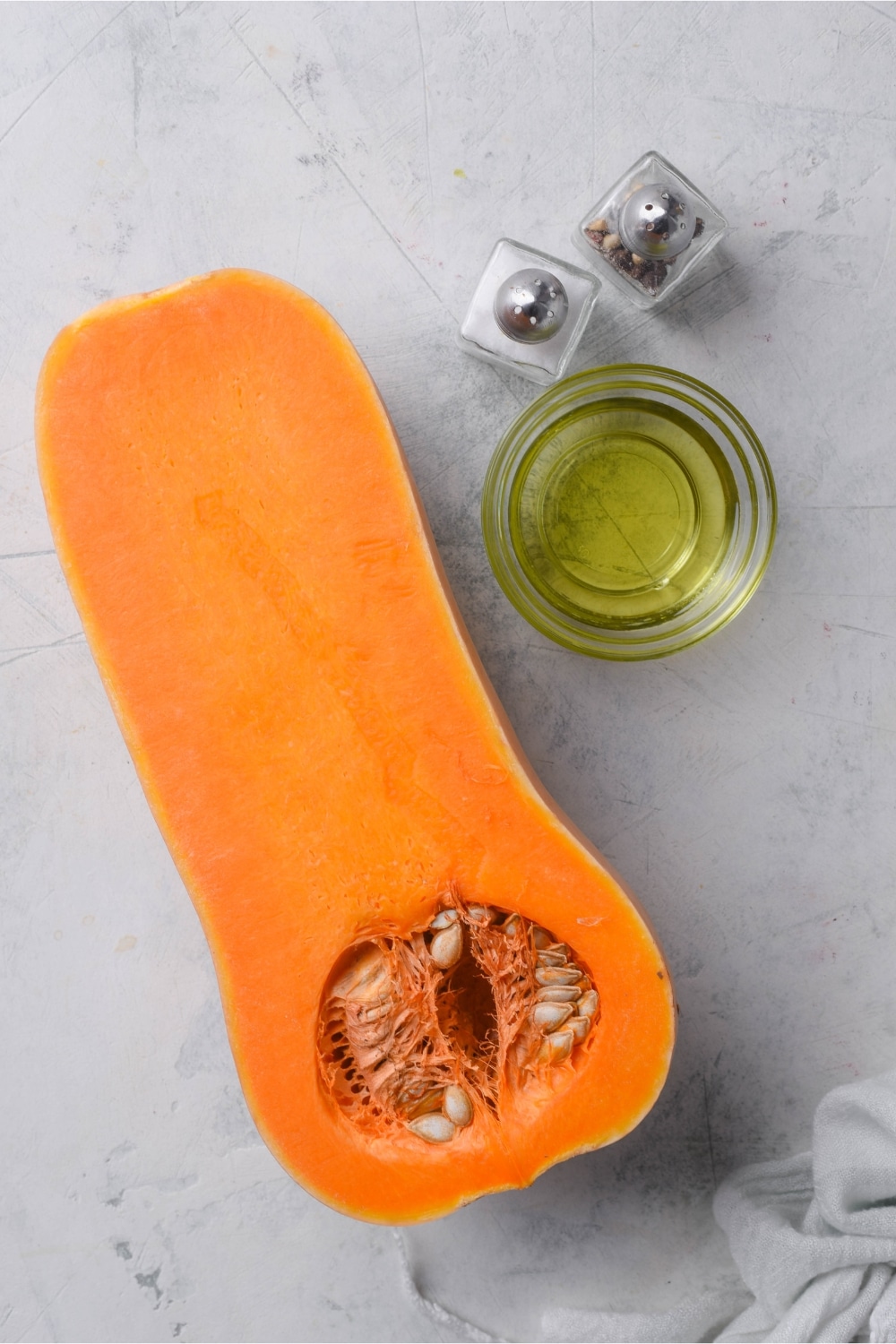 Half a butternut squash, a small glass bowl of oil, and salt and pepper shakers.