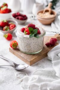 Overnight oats garnished with strawberries and raspberries in a glass served with two spoons.