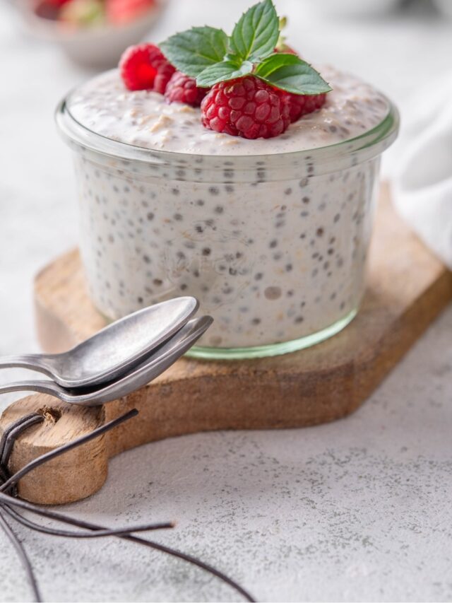 A small glass filled with overnight oats, topped with strawberries and raspberries next to two spoons.