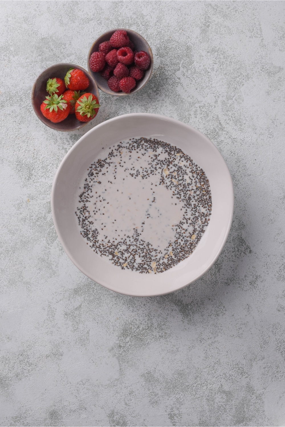 Prepared overnight oats mixture in a bowl next to bowls of strawberries and raspberries.