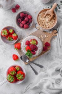 Top view of overnight oats in a glass surrounded by bowls of raspberries, strawberries, and rolled oats.