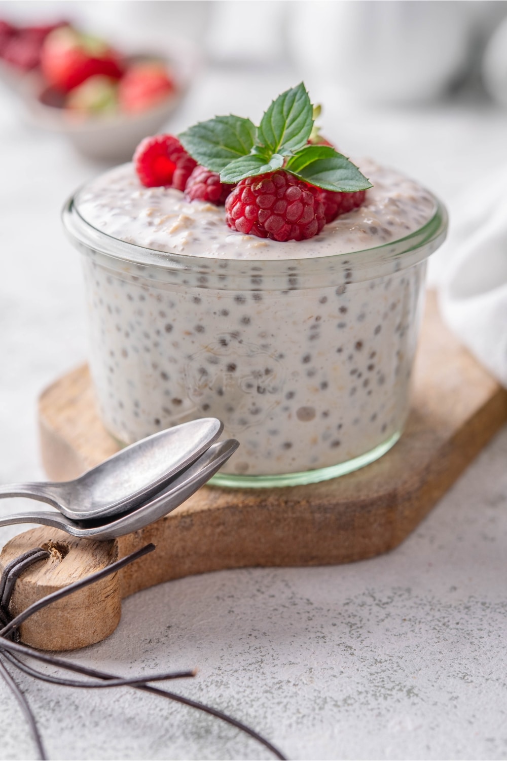 A small glass filled with overnight oats, topped with strawberries and raspberries next to two spoons.