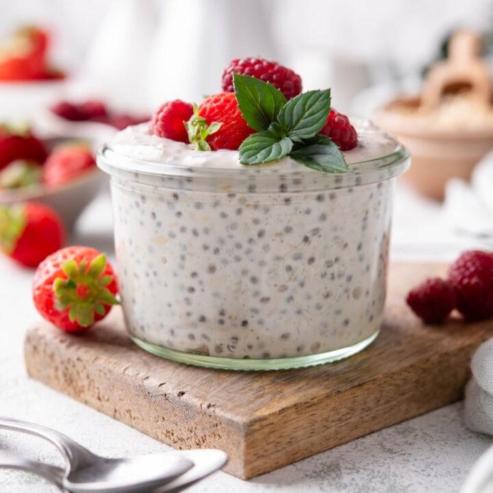 A small glass filled with overnight oats, topped with strawberries and raspberries.