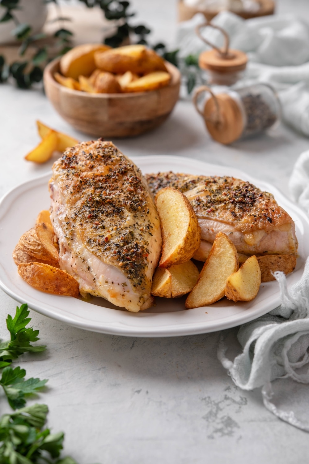 Two seasoned chicken breasts on a plate with potato wedges.