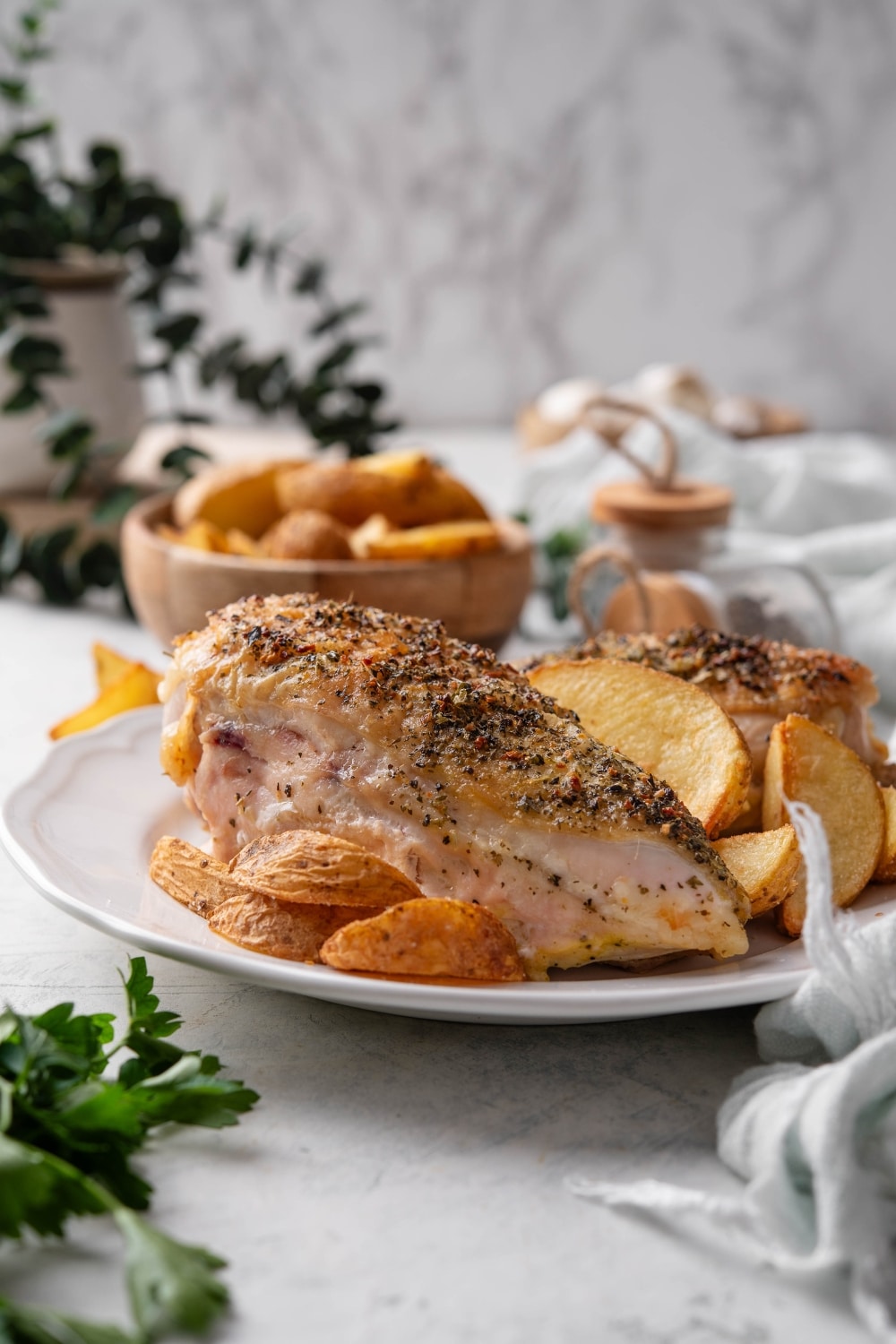 Two seasoned chicken breasts on a plate with potato wedges.