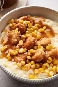A KFC bowl filled with mashed potatoes, chicken nuggets, corn kernels, and brown gravy.