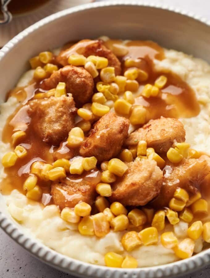 A KFC bowl filled with mashed potatoes, chicken nuggets, corn kernels, and brown gravy.