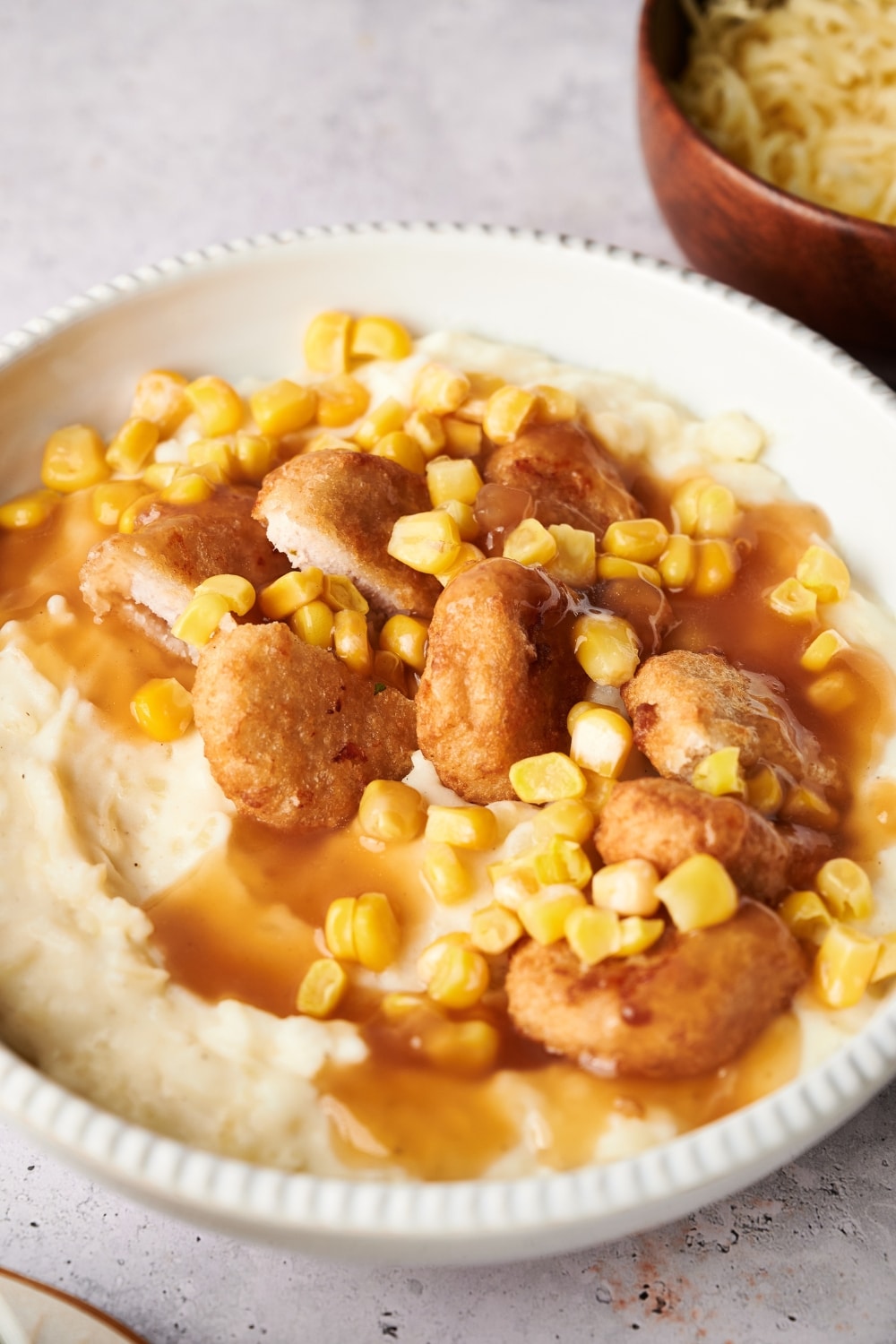 A KFC bowl filled with mashed potatoes, chicken nuggets, corn kernels, and brown gravy.