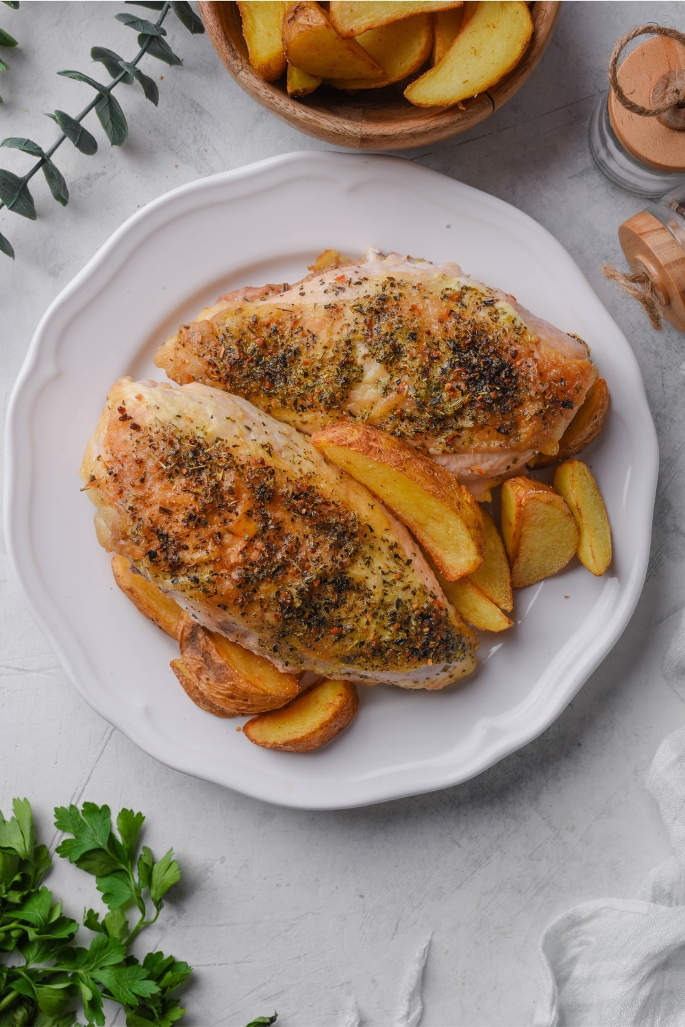 Two seasoned chicken breasts on a plate with potato wedges.