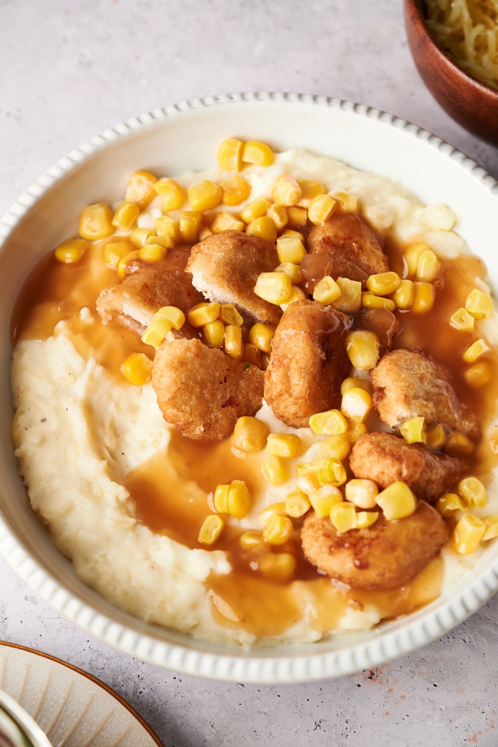 A KFC bowl filled with mashed potatoes, chicken nuggets, corn kernels, and brown gravy.