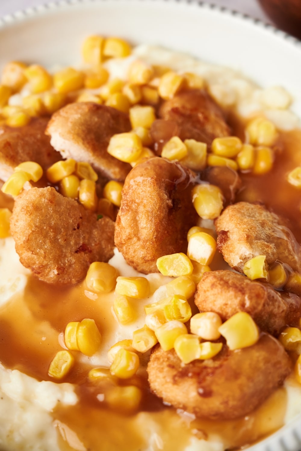 Close up of a KFC bowl filled with mashed potatoes, chicken nuggets, corn kernels, and brown gravy.