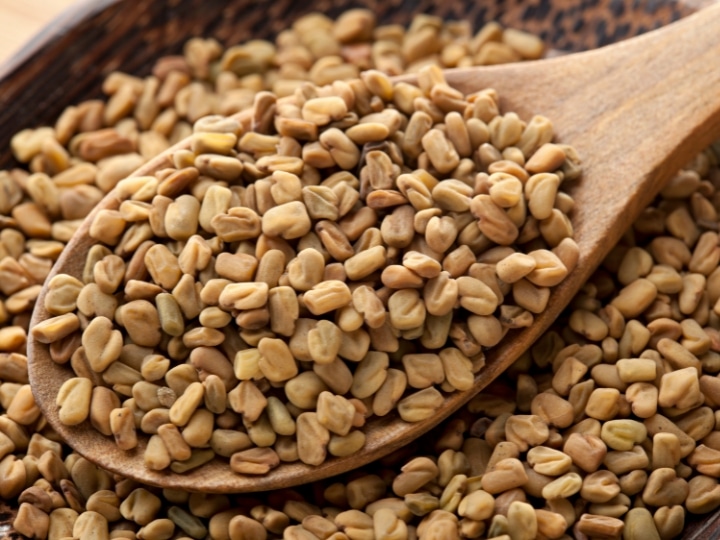 A bunch of Fenugreek on a wooden spoon in a bowl of Fenugreek.