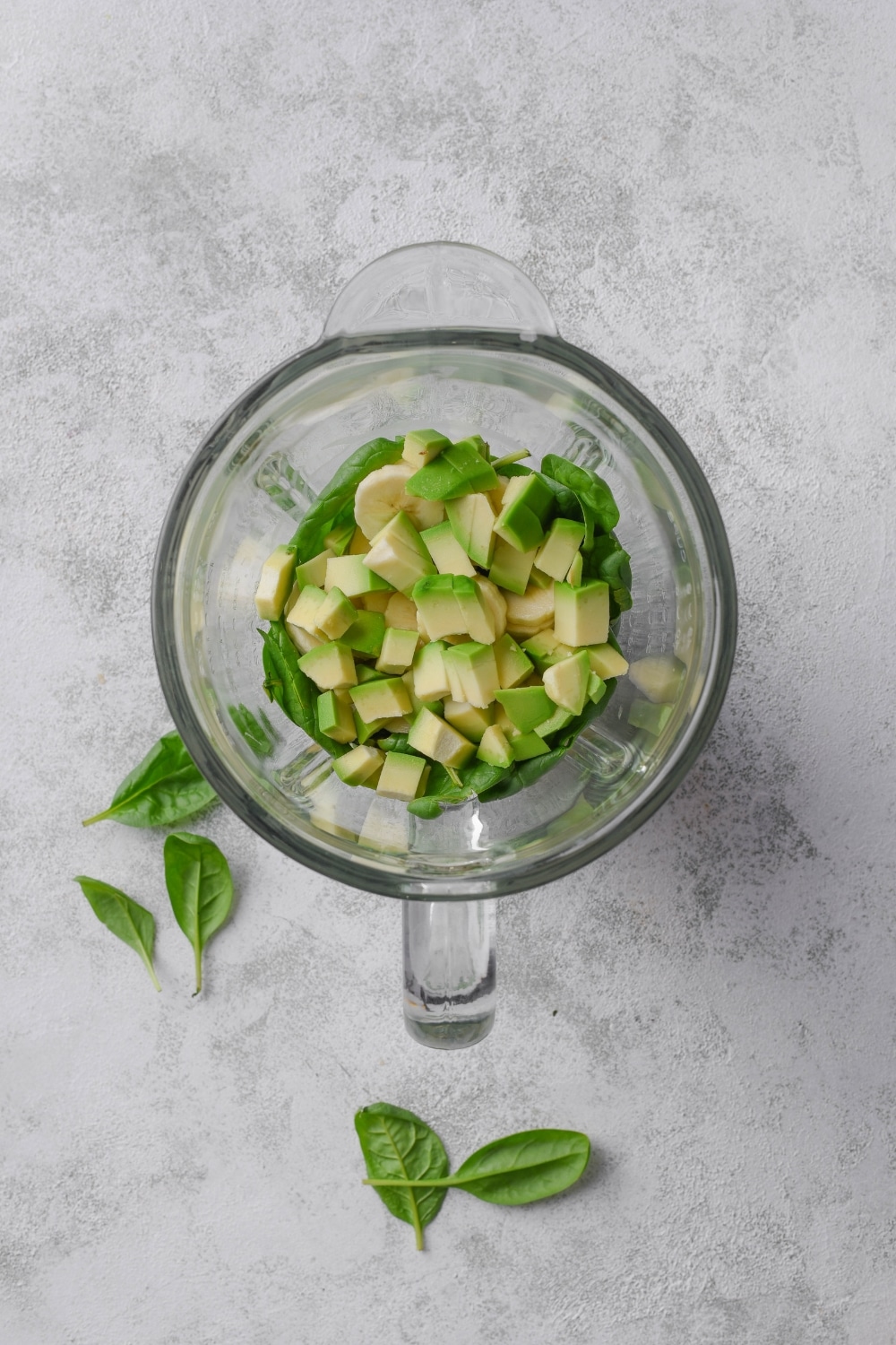 A blender filled with spinach and diced avocado.