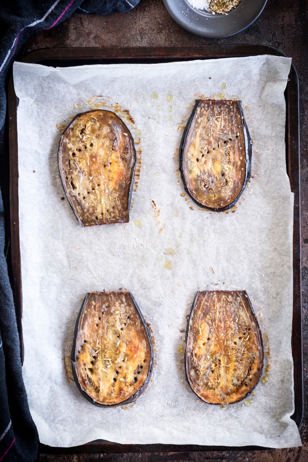 A baking sheet lined with parchment paper with four eggplant slices on it.