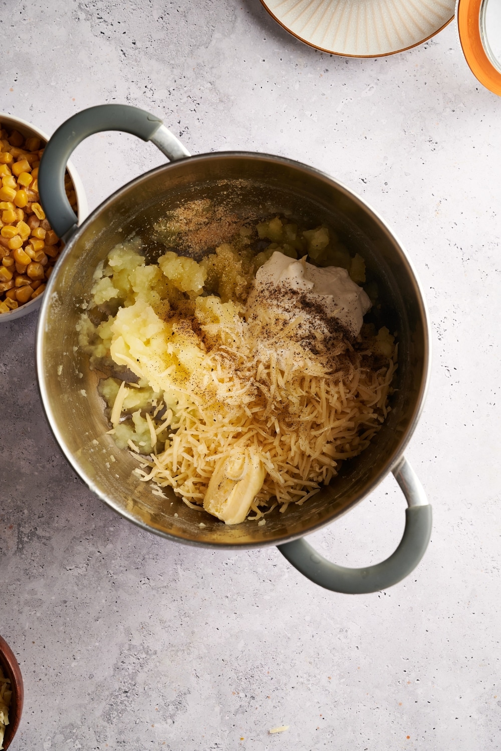 A pot filled with mashed potatoes, shredded cheese, cream cheese, butter, and seasonings.