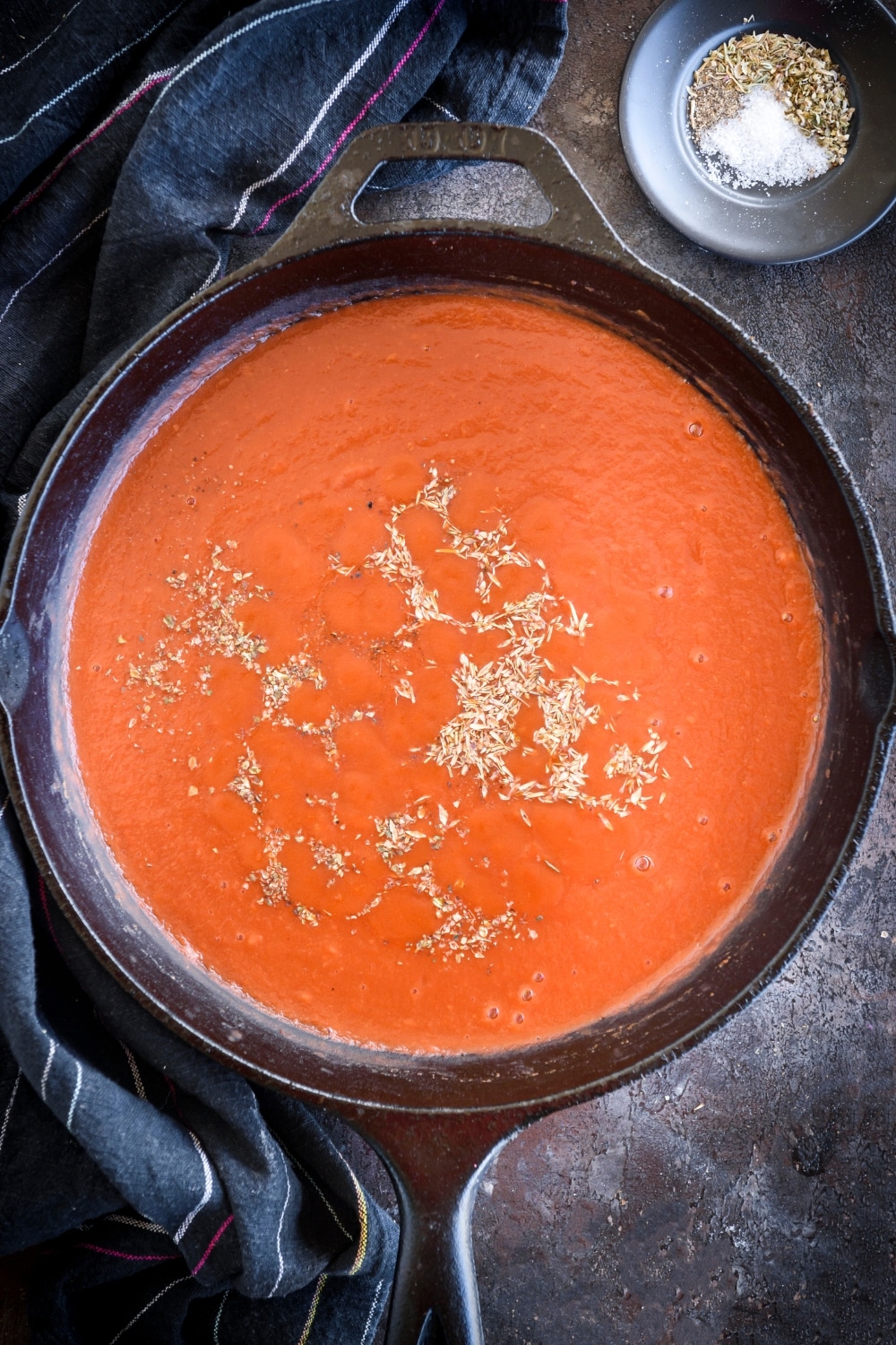 A cast iron skillet filled with tomato sauce and seasonings.