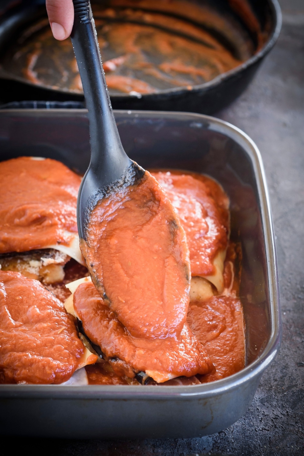 A spoon of red sauce being poured over a baking dish filled with unbaked chicken Sorrentino.