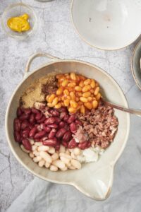 A bowl filled with canned baked beans, kidney beans, butter beans, seasonings, and ground beef.