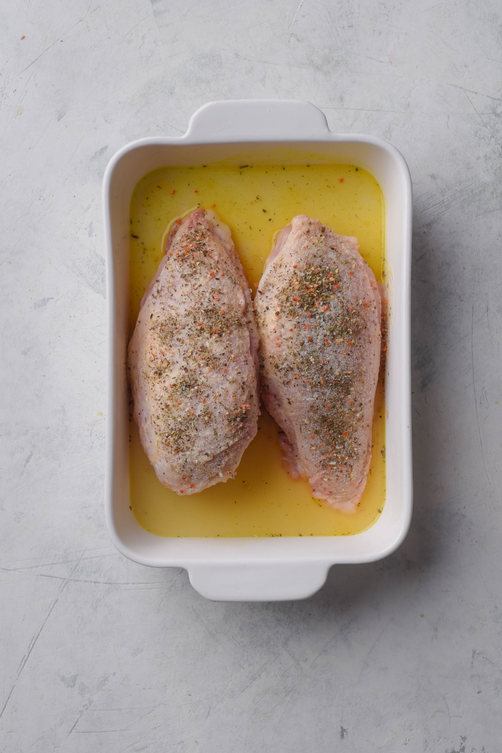 A baking dish with chicken broth and two raw seasoned chicken breasts in it.