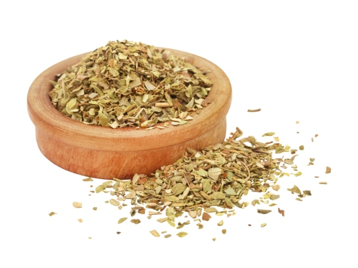 A wood bowl of oregano with some oregano in front of it.