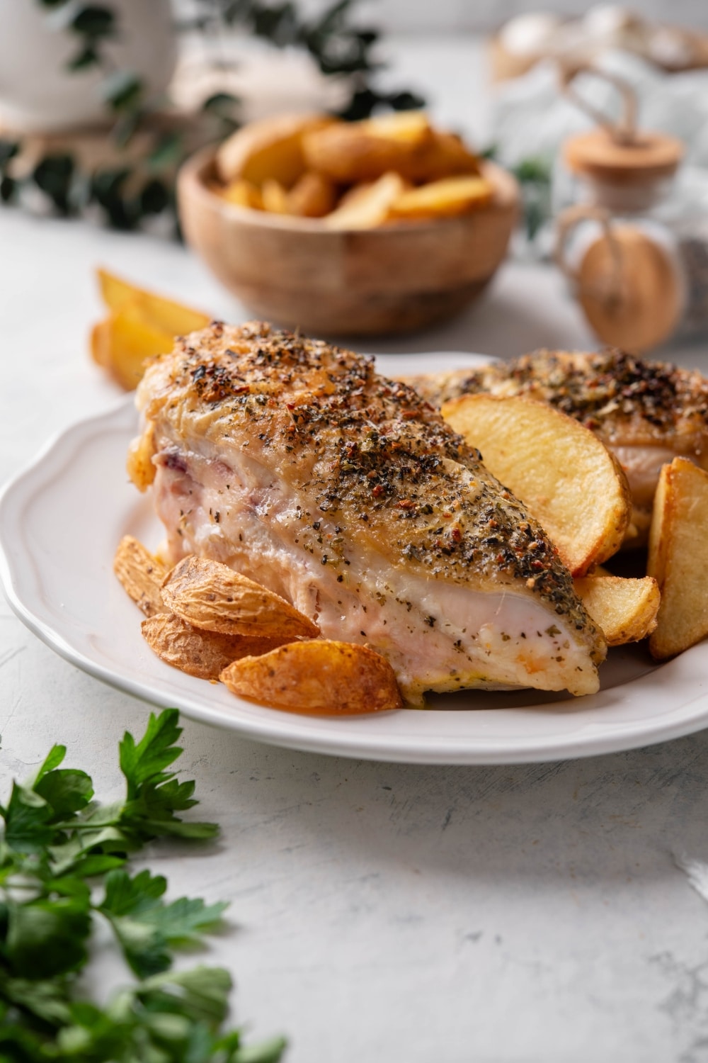 Two seasoned chicken breasts on a plate with potato wedges.