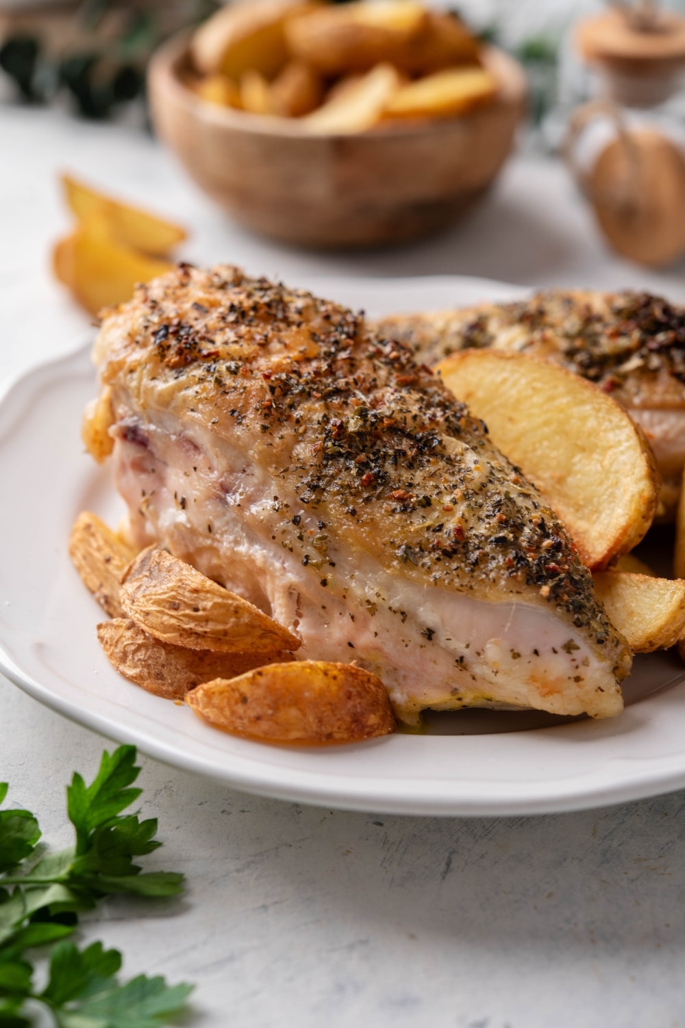 Two seasoned chicken breasts on a plate with potato wedges.