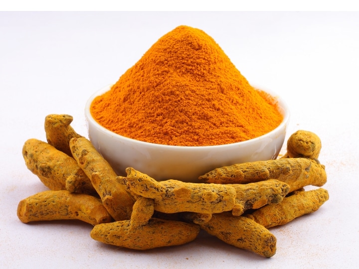 A mound of turmeric in a white bowl with some turmeric root in front of it.