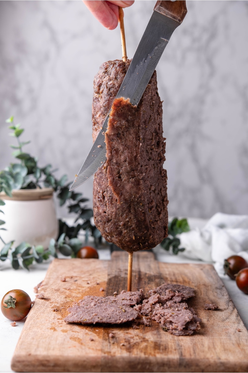 A log of beef being sliced into thin strips using a sharp knife.