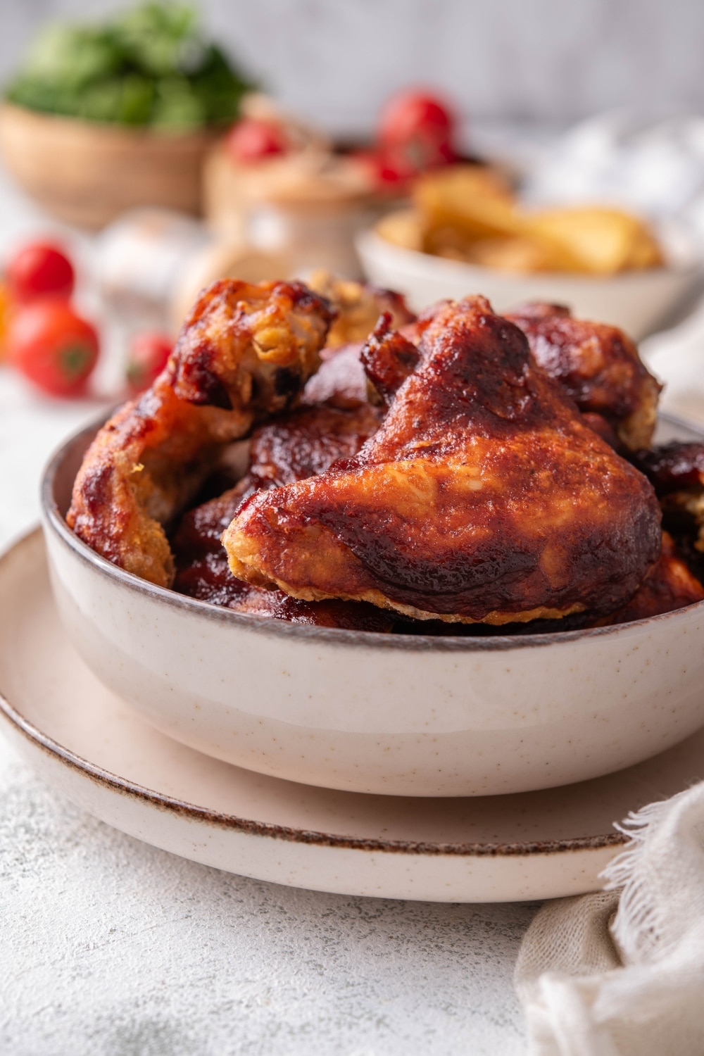 Part of a white bowl that is filled with bbq chicken wings. The bowl is on a white plate on a grey counter.