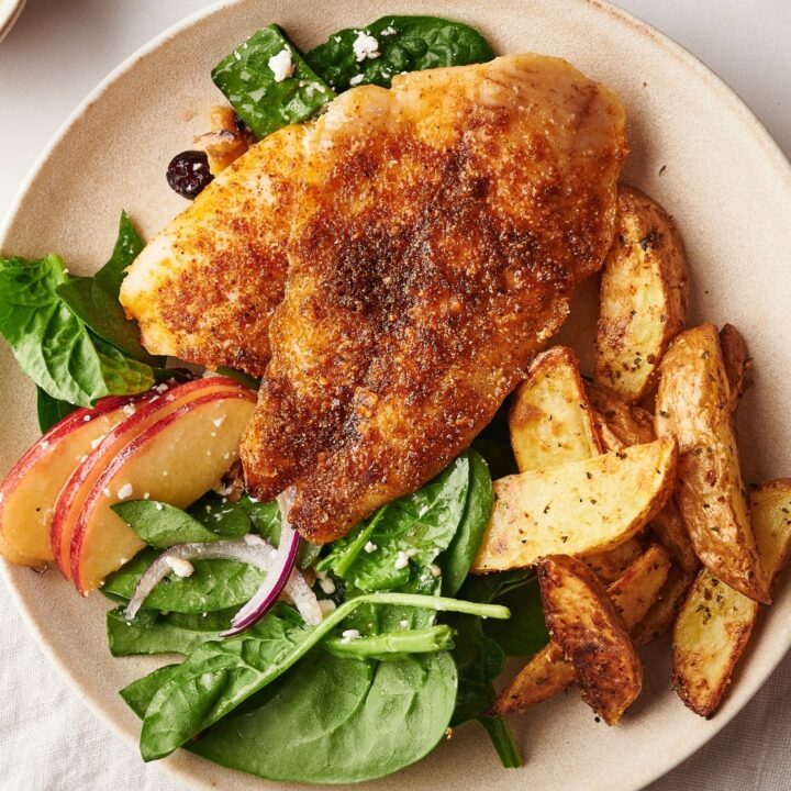 A piece of catfish on top of potatoes and spinach on a white plate.