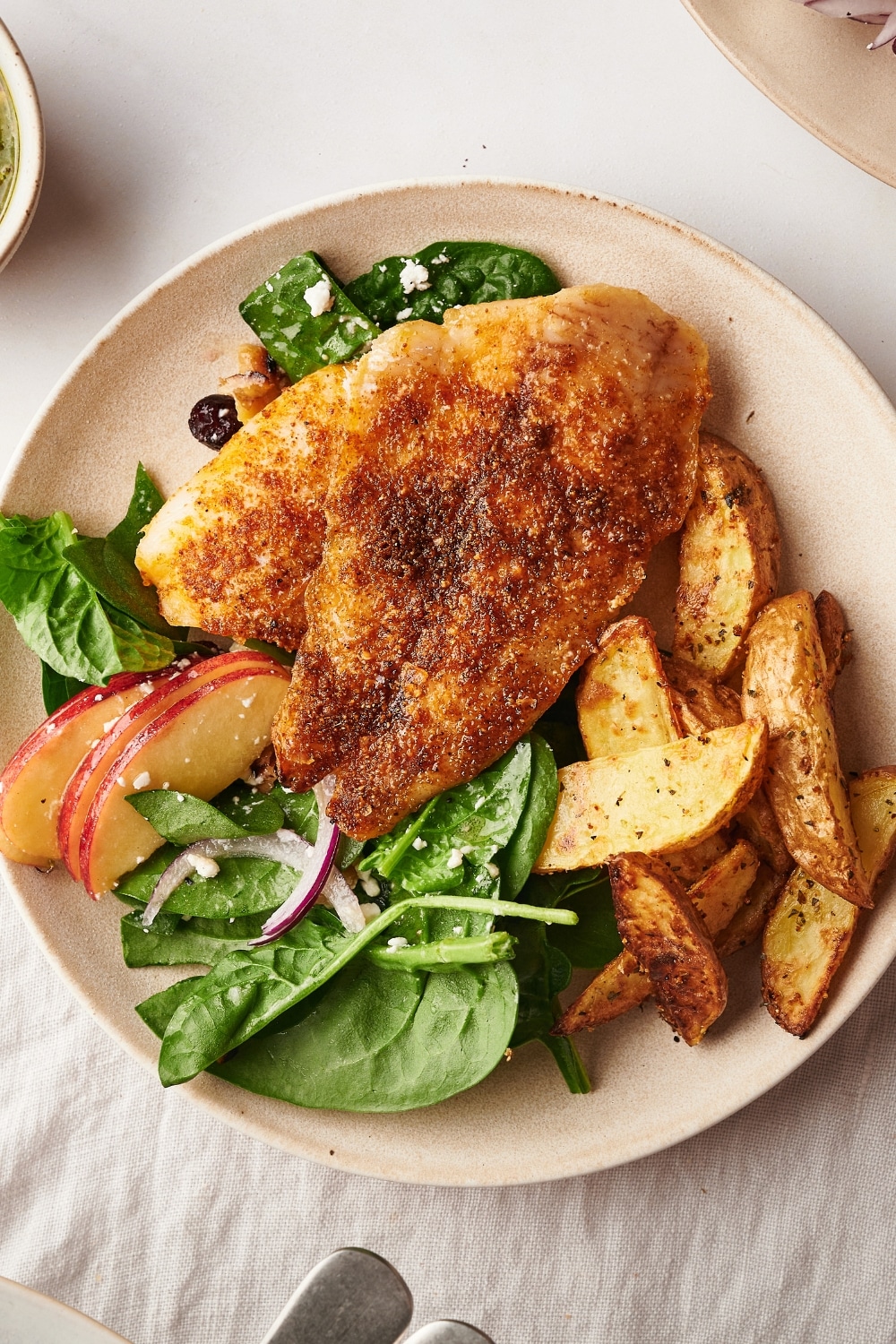 A piece of catfish on top of potatoes and spinach on a white plate.