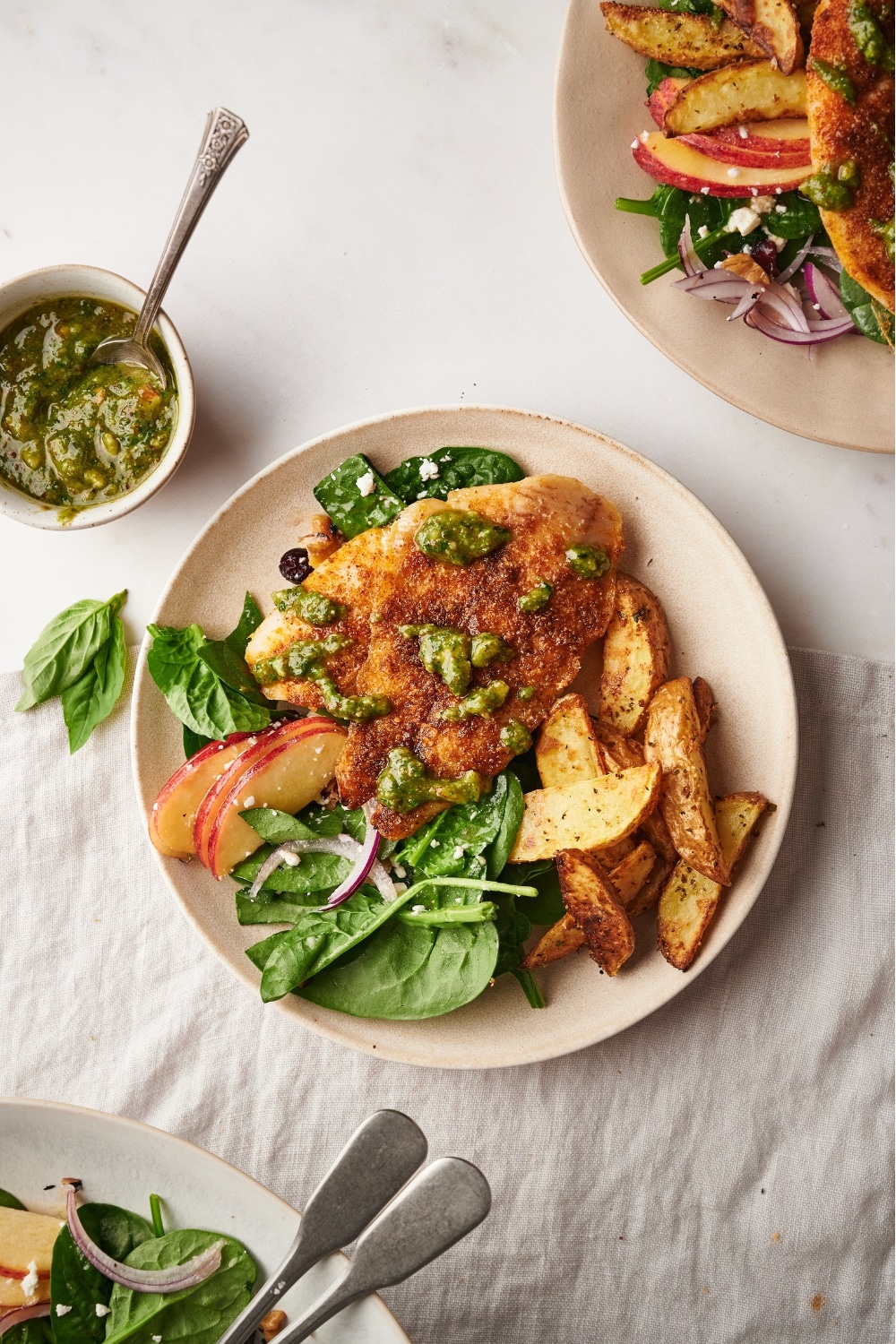 Pesto on top of catfish on top of potatoes and spinach on top of a white plate.