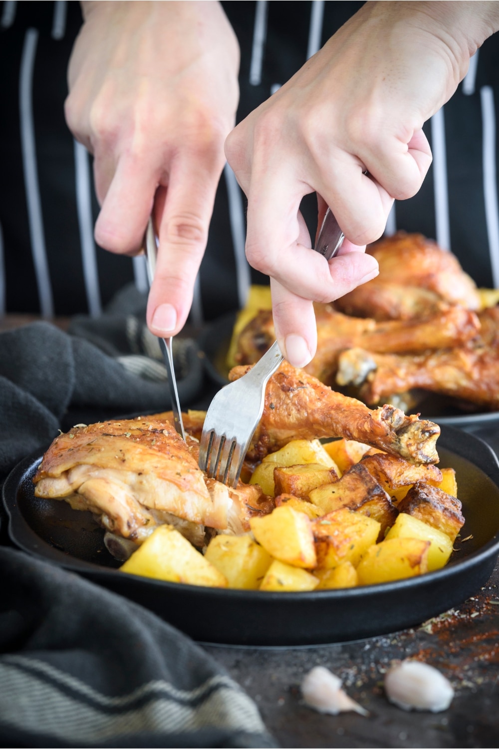 Two hands cutting chicken with potatoes on a plate.