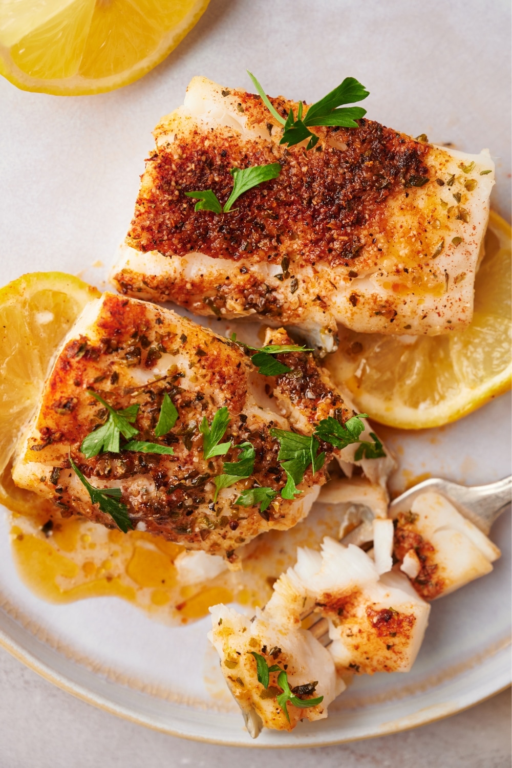 Two seasoned mahi mahi fillets on top of lemon slices on a white plate.