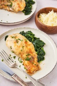 A piece of mushroom chicken with collard greens on a white plate with a fork.