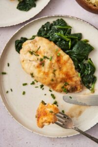A fork with a piece of chicken on it on a plate with the rest of the chicken breast on the plate.